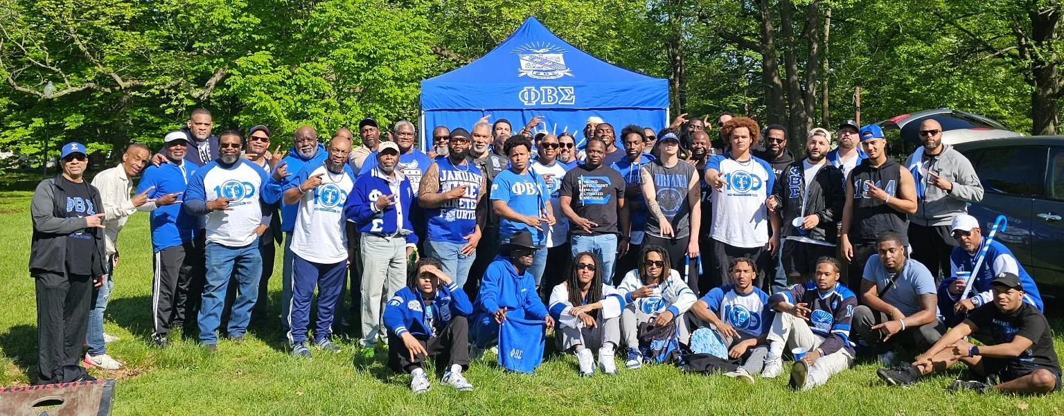 Tau Chapter brothers gathered outdoors beneath a blue Phi Beta Sigma tent